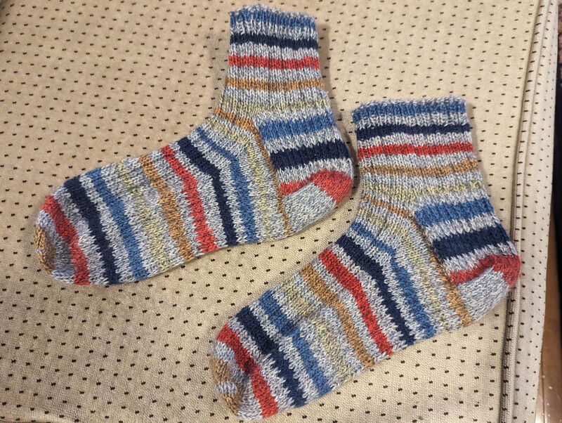Image of the completed pair of socks lying side-by-side on our loveseat.